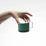 Hand holding a green mug of brewed Blue Lullaby butterfly pea tea