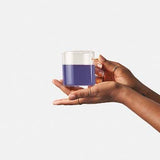 Small glass of naturally blue-purple brewed Minty Blue tea held in hand