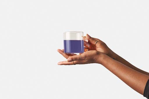 Small glass of naturally blue-purple brewed Minty Blue tea held in hand