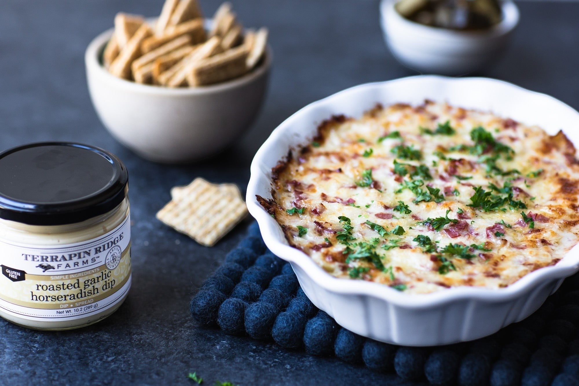 Baked Roasted Garlic Horseradish Dip in a white dish with crackers and pickles