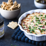 Baked Roasted Garlic Horseradish Dip in a white dish with crackers and pickles
