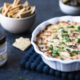 Baked Roasted Garlic Horseradish Dip in a white dish with crackers and pickles