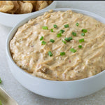 Bowl of Hatch Chile Cream Cheese Dip topped with green onions, with pork rinds and celery