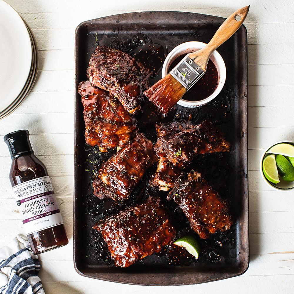 Ribs glazed with Raspberry Peach Chipotle Sauce with a basting brush and lime wedges