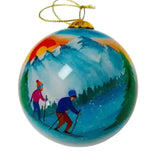 Glass ornament painted with a couple skiing down a snowy slope under an orange sunset