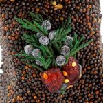 Close-up of dark seed ornament topped with juniper sprigs and red cranberries