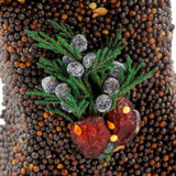 Close-up of dark seed ornament topped with juniper sprigs and red cranberries