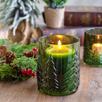 Green embossed glass candle holder with a lit candle among greenery