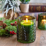 Green embossed glass candle holder with a lit candle among greenery