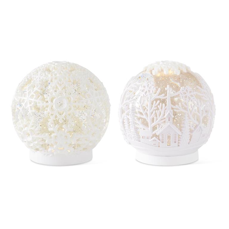 Two white acrylic globes, one with snowflake cutouts and one with a cutout winter village scene