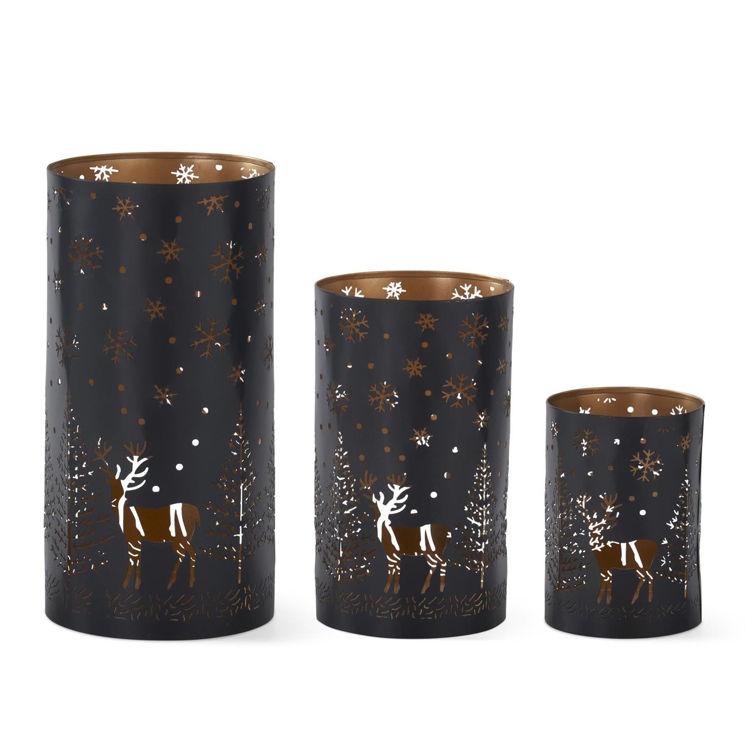 Three black metal cylinder lanterns with deer, tree and snowflake cutouts and copper-toned interiors