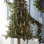 Tall lit Christmas tree by a staircase hung with many flickering taper candles