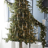 Tall lit Christmas tree by a staircase hung with many flickering taper candles