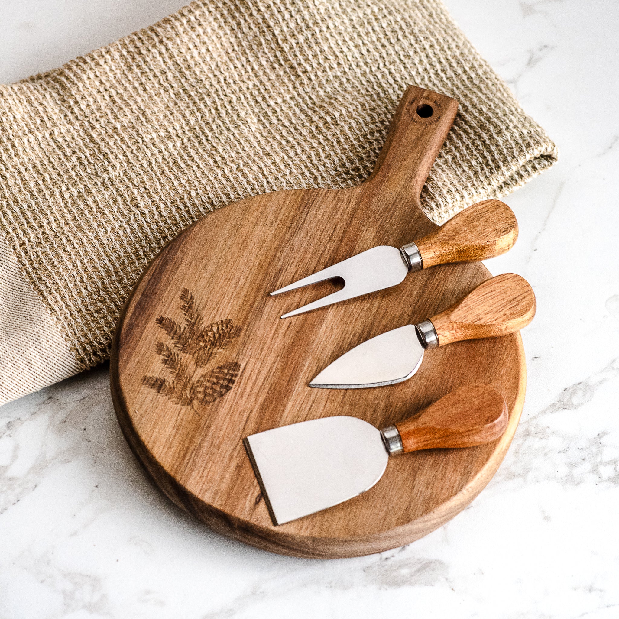Round wood cheese board with engraved evergreen and three cheese knives