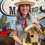 Woman in a straw hat holding a juniper seed-covered birdhouse