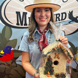 Woman in a straw hat holding a juniper seed-covered birdhouse