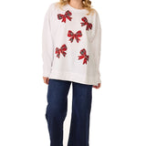 Model in a white sweatshirt with scattered red sparkle bows, jeans, and black boots