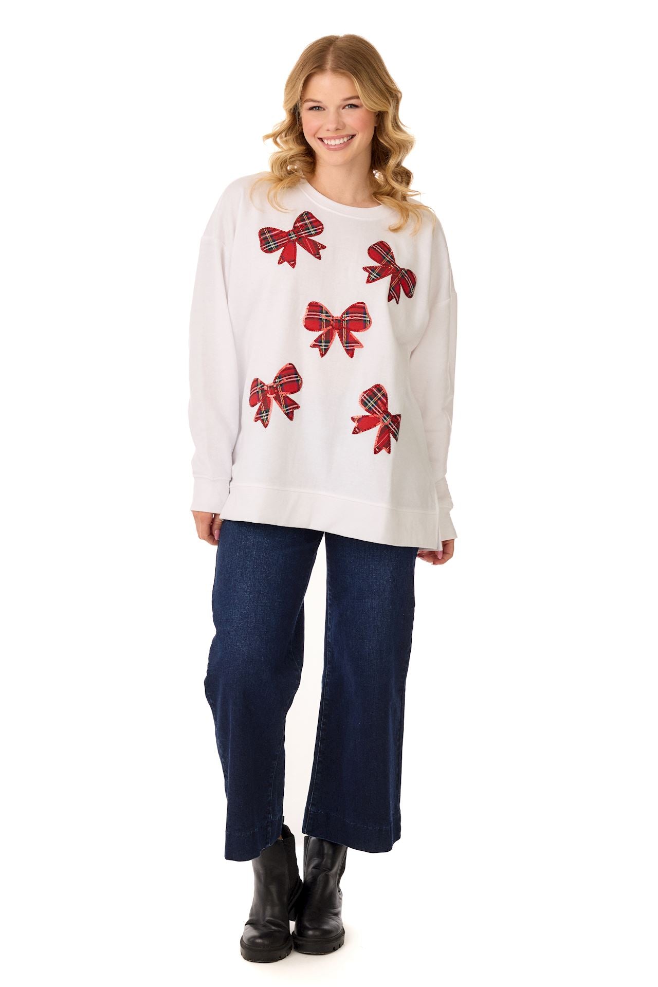 Model in a white sweatshirt with scattered red sparkle bows, jeans, and black boots