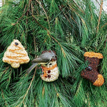 Seed tree, snowman, and boot ornaments hanging on jute in a pine tree with a chickadee