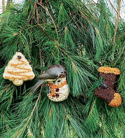 Seed tree, snowman, and boot ornaments hanging on jute in a pine tree with a chickadee