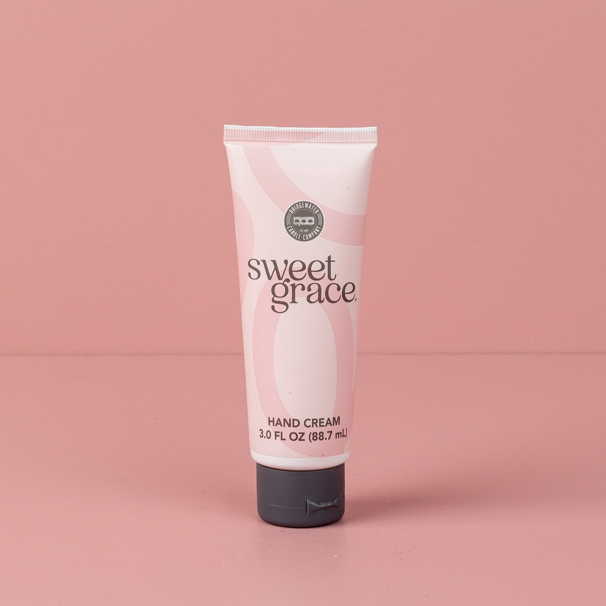 Sweet Grace Hand Cream tube with flip-top cap standing on a pink surface
