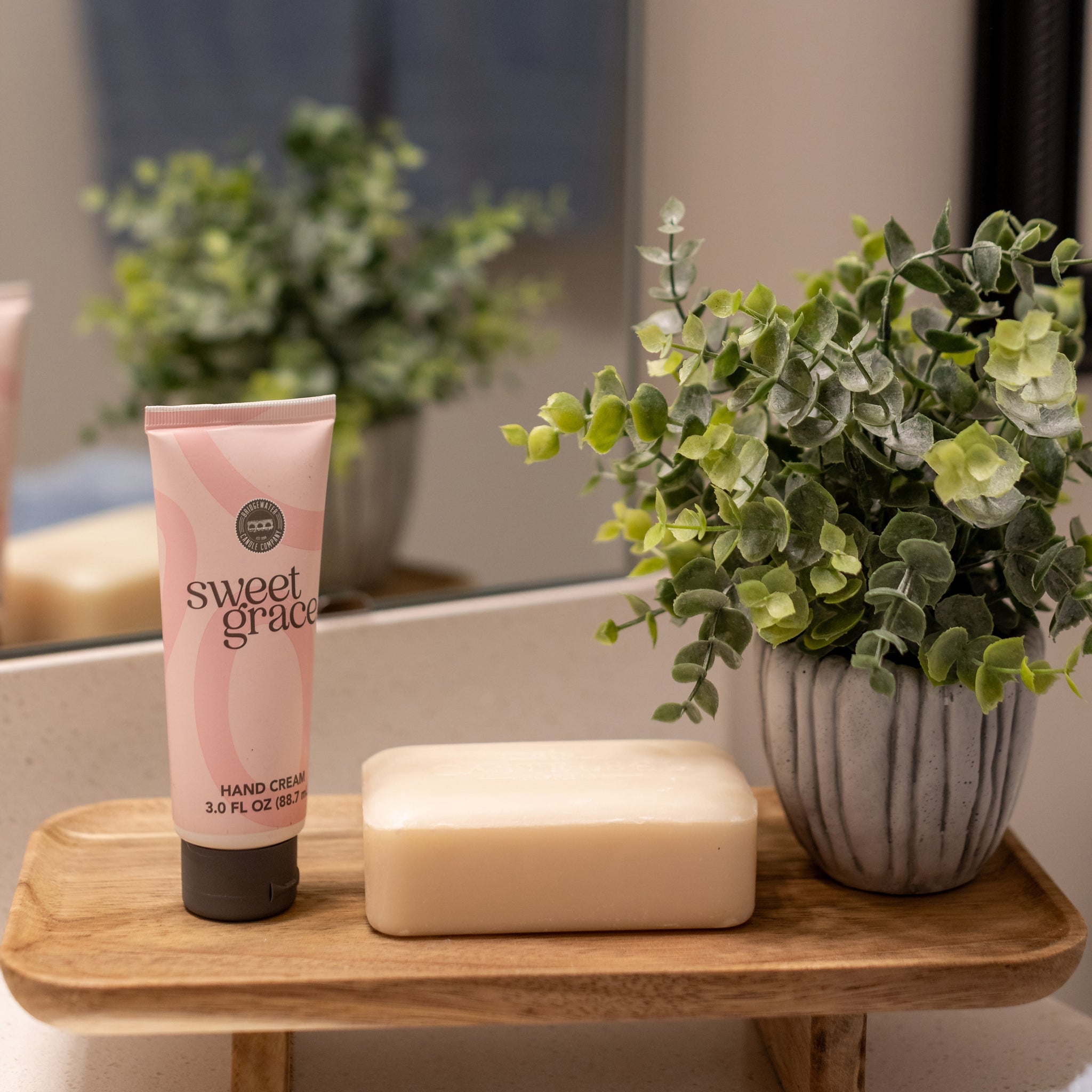Sweet Grace Hand Cream styled on a wooden tray on a bathroom counter with soap and a small plant