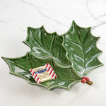Green ceramic holly leaf plate with red berry accents holding a wrapped chocolate on marble