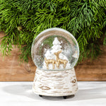 Musical snow globe with gold deer and white trees inside, on a white birch-bark style base