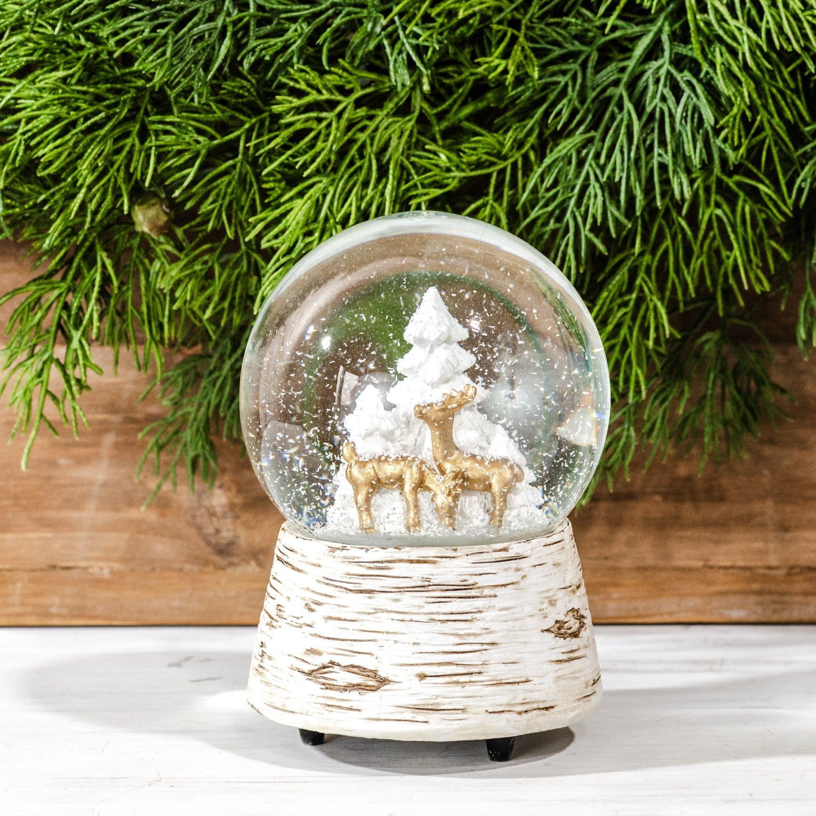 Musical snow globe with gold deer and white trees inside, on a white birch-bark style base