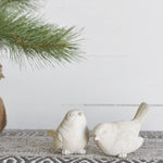 Two small cream-white textured bird figures, one with its tail raised, on a woven runner