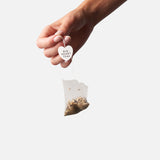 Hand dropping a Big Heart Tea compostable green tea bag