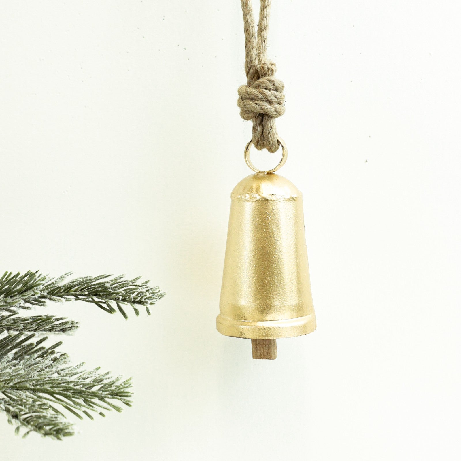 Brushed gold cowbell hanging from a knotted jute rope beside a pine branch