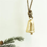 Small gold cowbell on a knotted jute rope hanger against a white backdrop with pine sprigs
