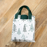 White gift bag with green handles and a sketched evergreen tree print holding folded kitchen towels