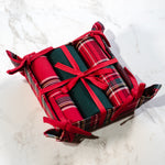 Three red tartan and green kitchen towels tied with red ribbon in a matching plaid fabric basket