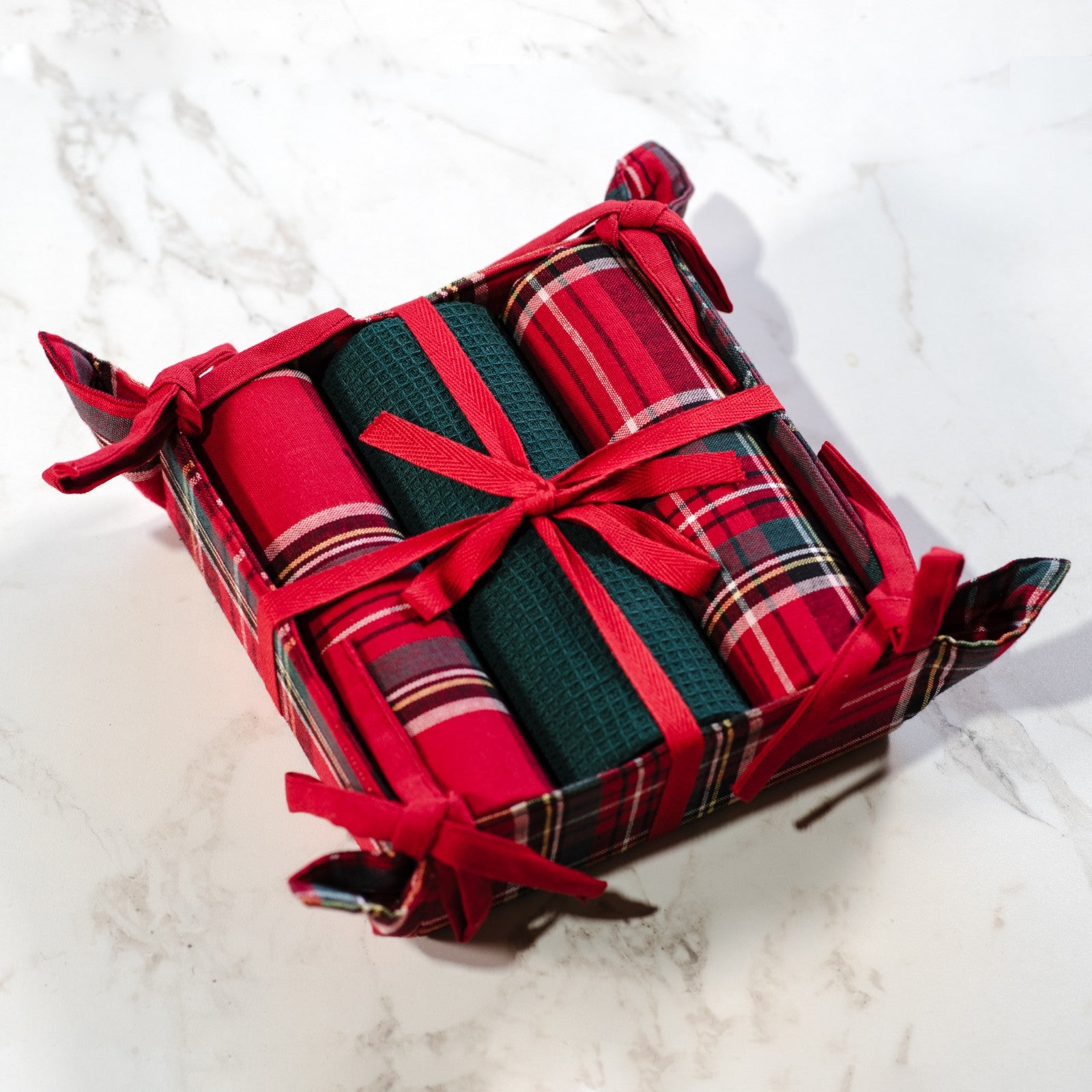 Three red tartan and green kitchen towels tied with red ribbon in a matching plaid fabric basket