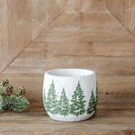 Small white textured planter with a band of green evergreen trees, on a wood shelf