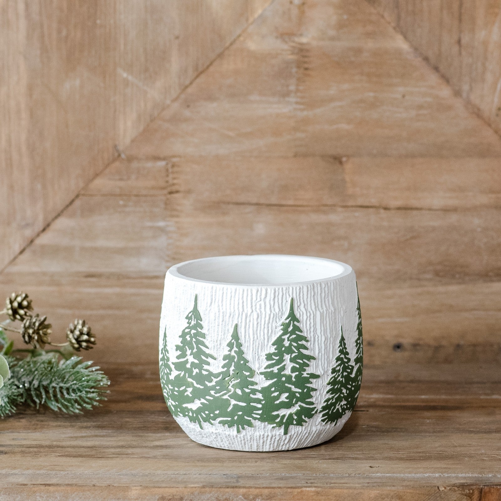 Small white textured planter with a band of green evergreen trees, on a wood shelf