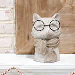 Gray cement fox vase wearing round black eyeglasses and a knit-look scarf on a white shelf