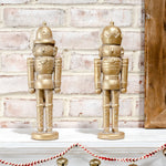 Two gold nutcracker figures standing on a white mantel above a red and white striped rope