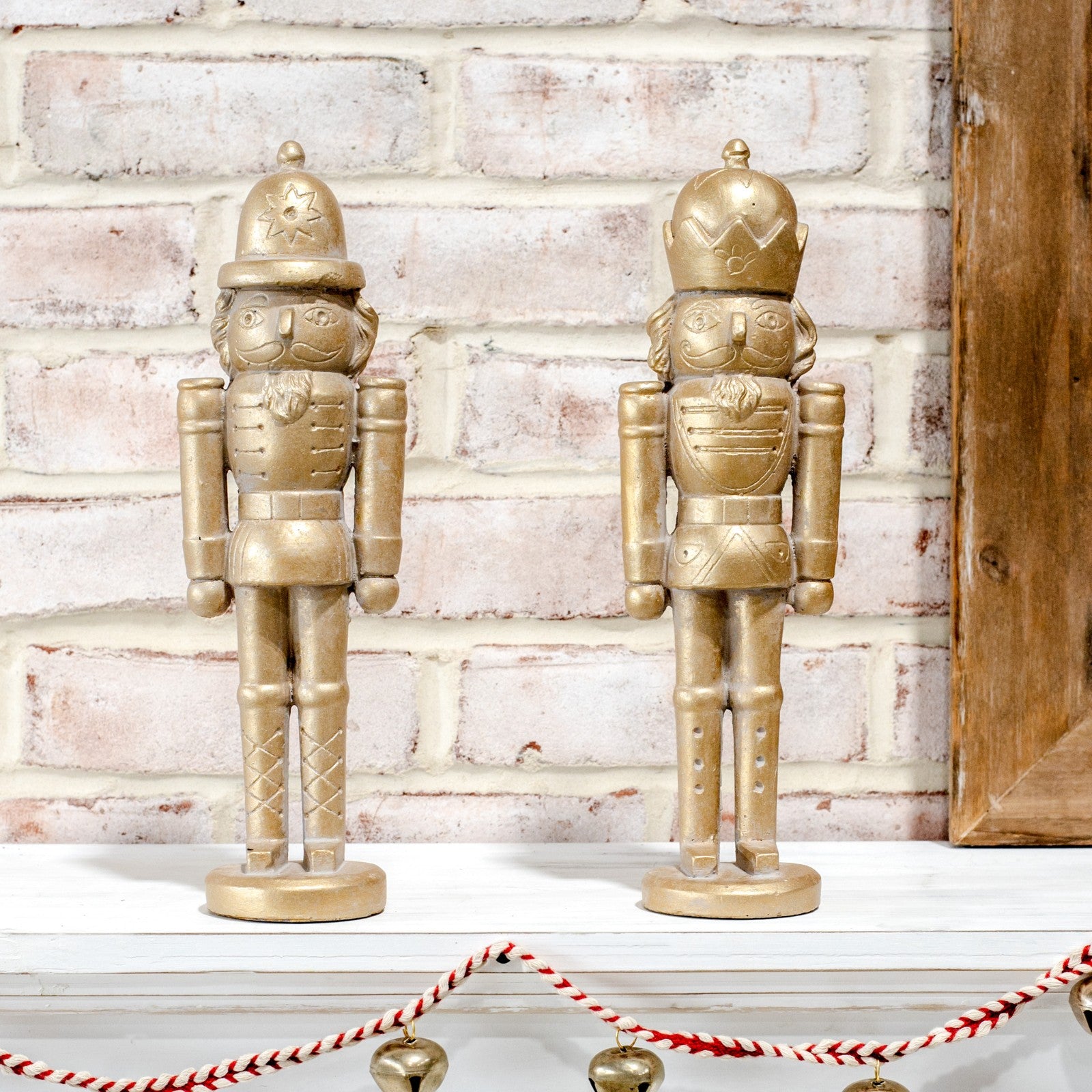 Two gold nutcracker figures standing on a white mantel above a red and white striped rope