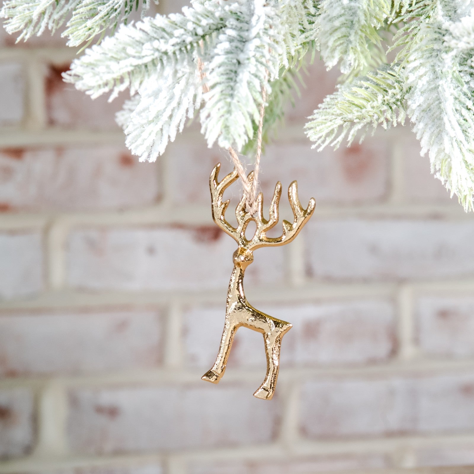 Tiny gold metal reindeer ornament with branching antlers hanging from a frosted pine branch