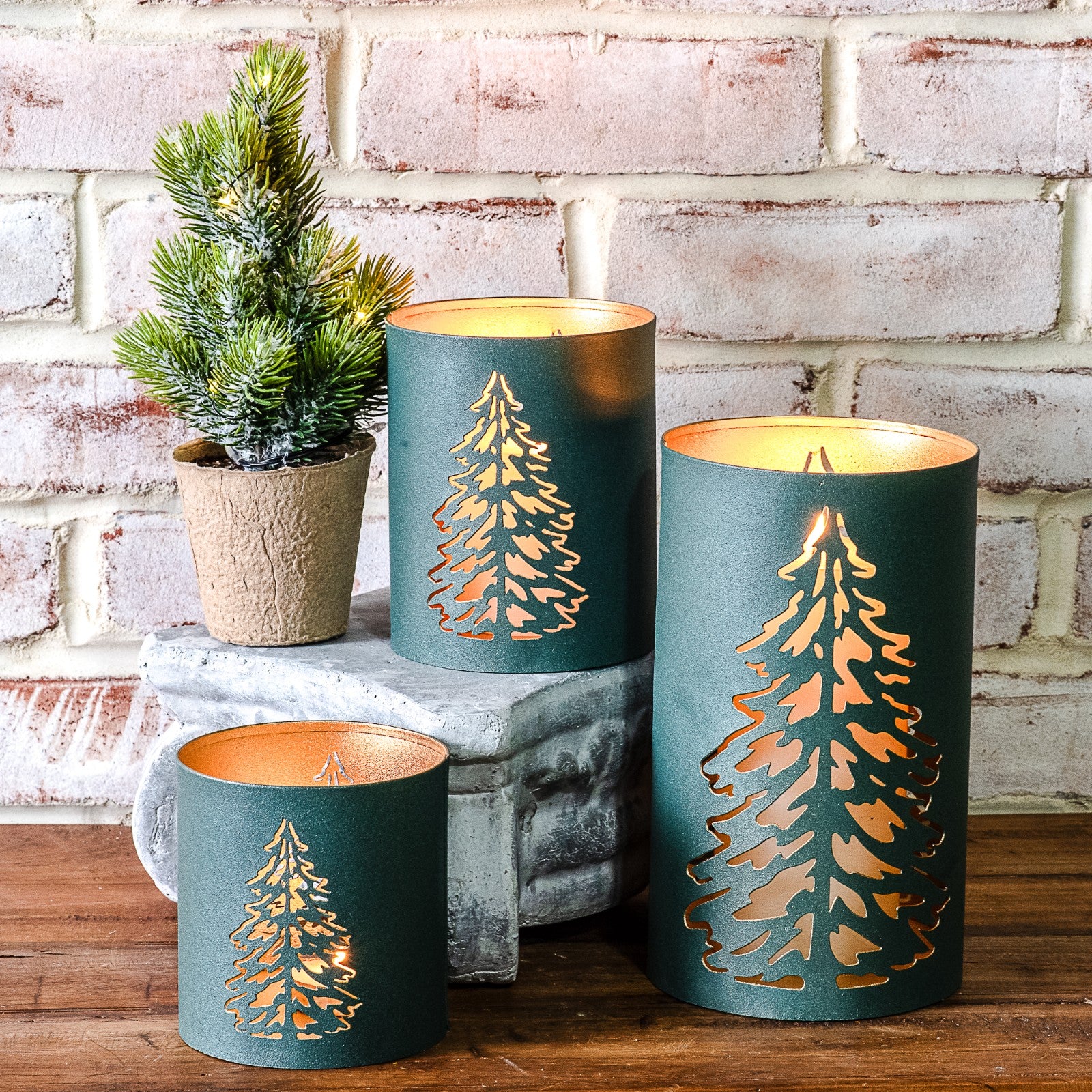 Teal green metal lanterns with gold cut-out Christmas tree designs glowing from inside