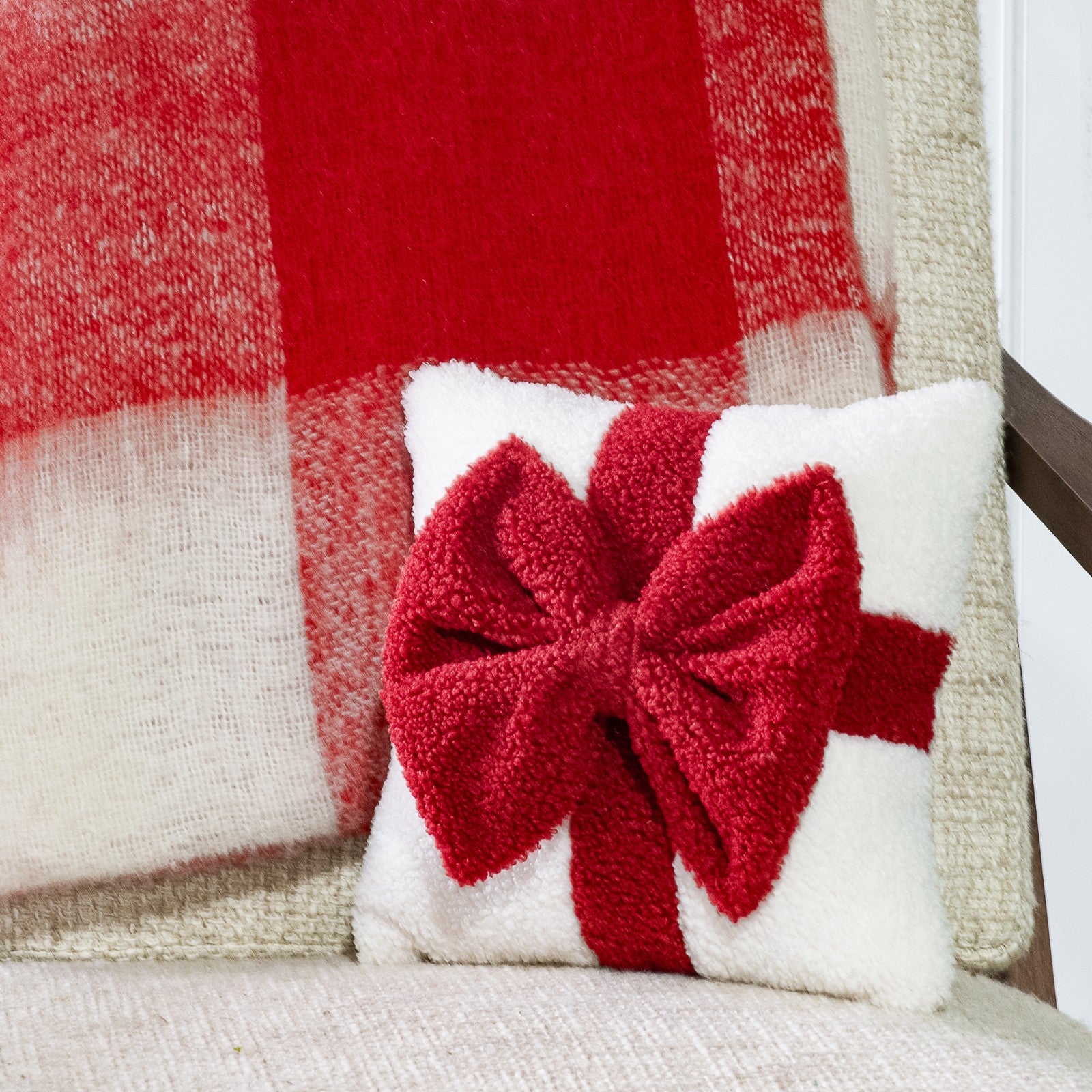 Small white textured pillow with a plush red bow and ribbon band, set against a red plaid throw