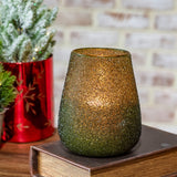 Green beaded glass votive holder with a lit candle glowing through its textured surface