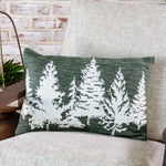 Green lumbar pillow with a row of white evergreen tree silhouettes on a cream upholstered chair
