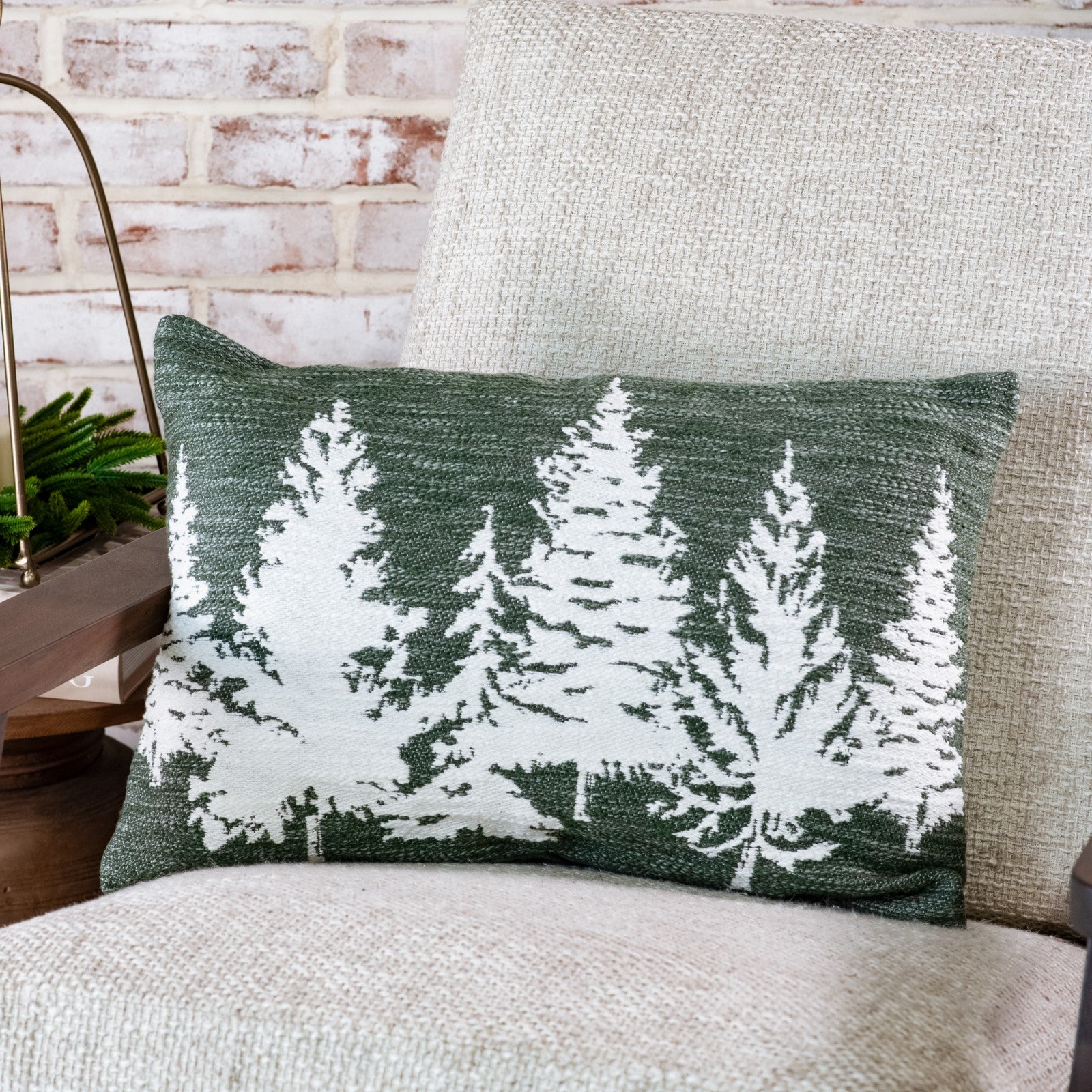 Green lumbar pillow with a row of white evergreen tree silhouettes on a cream upholstered chair