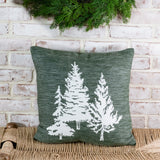 Heathered green square pillow with three white evergreen tree silhouettes on a woven bench