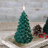 Dark green tree-shaped wax LED candle with a flickering flame on a wood tray with pinecones