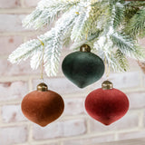 Velvet teardrop ornaments in deep green, rust and red with gold caps hanging from a flocked branch